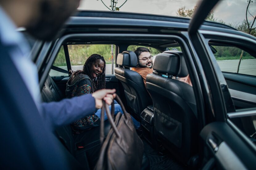 Group of people sharing a ride together in the car; one person is getting inside the back...