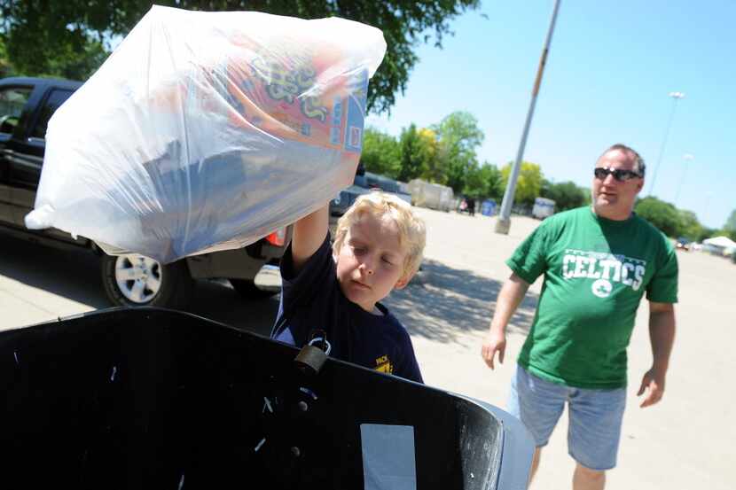 Sam Dee, 7, from Rowlett, throws away paper products while his father, Kenny, watches on...