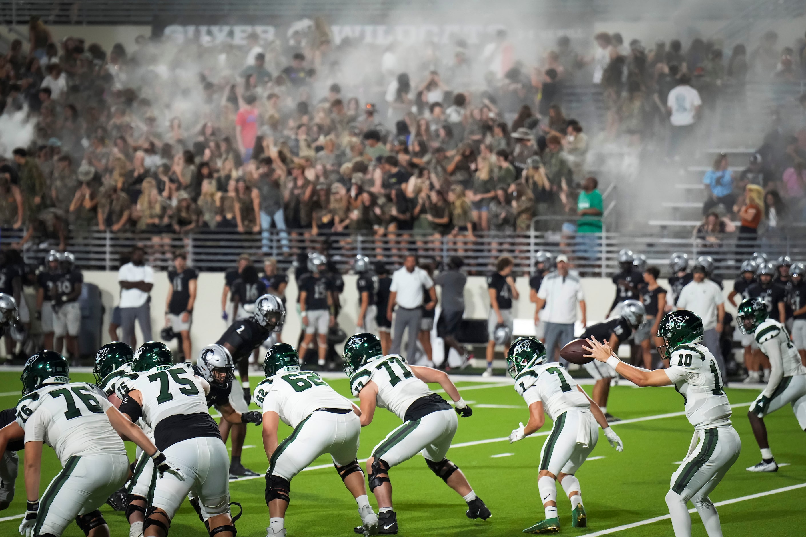 Prosper quarterback Harrison Rosar (10) takes a snap as Denton Guyer students celebrate in a...