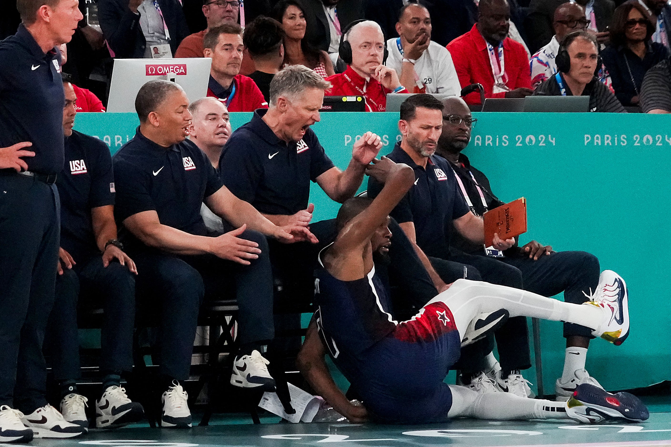 Kevin Durant (7) of the United States tumbles into his team’s bench at the feet of coach...