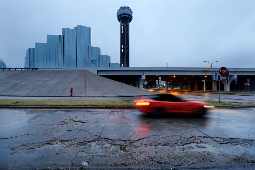 A car pass through broken up concrete and rain-water filled potholes near Reunion Tower in...