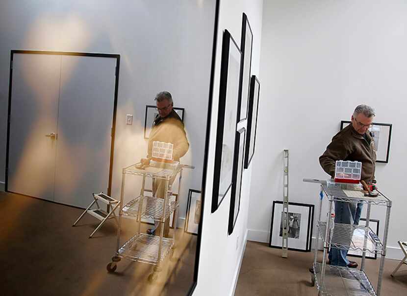  Burt Finger is reflected in a Keith Carter piece as he hangs Some Bill Owens work at...