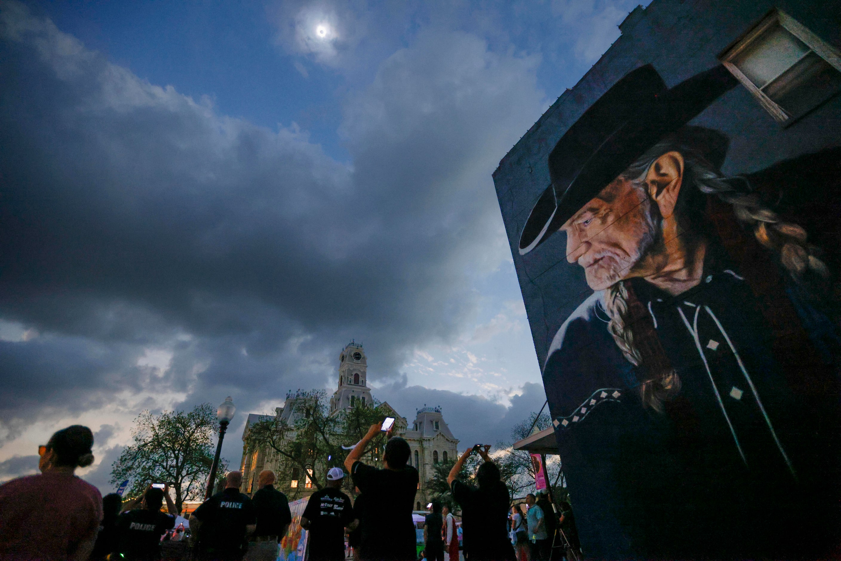 People watch a total solar eclipse over the Hill County Courthouse and a mural of Willie...