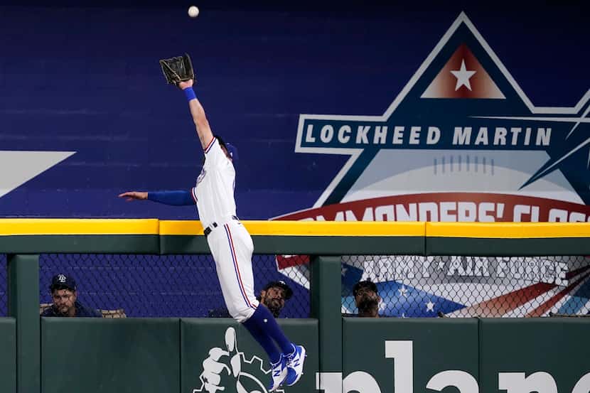 Texas Rangers center fielder Eli White leaps to the top of the wall to catch a flyout by...