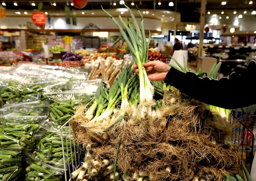 A shopper selects green onions at H Mart. 