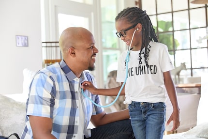 African American man kneels next to child in a t-shirt that reads "Live United" as she holds...