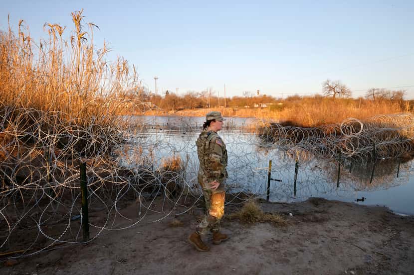 Texas National Guard Spc. Victoria Morgan walks by razor wire along the Rio Grande at Shelby...