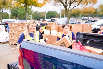 Three women help to load a pickup truck bed with boxes for a food pantry.