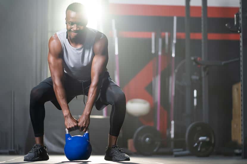 An adult black man swings a kettlebell inside of a fitness gym.