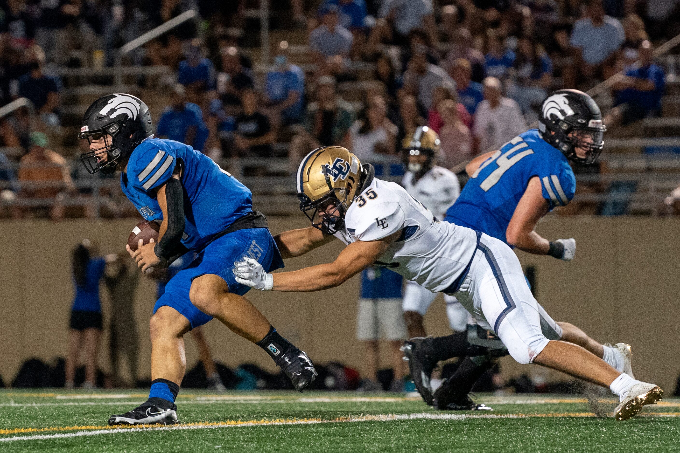 Plano West junior quarterback Vance Feuerbacher (19) tries to escape the tackle of Little...