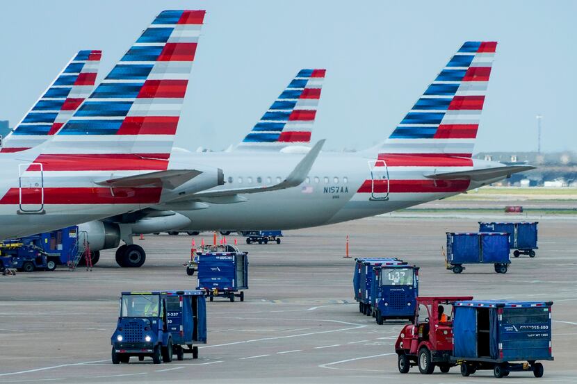 Baggage carts drive on the tarmac near American Airlines planes at the gates of Terminal C...