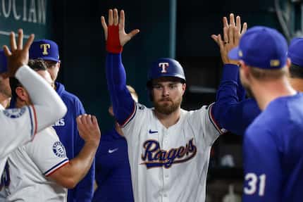 Texas Rangers first baseman Jared Walsh (21) high fives his teammates after scoring a run...