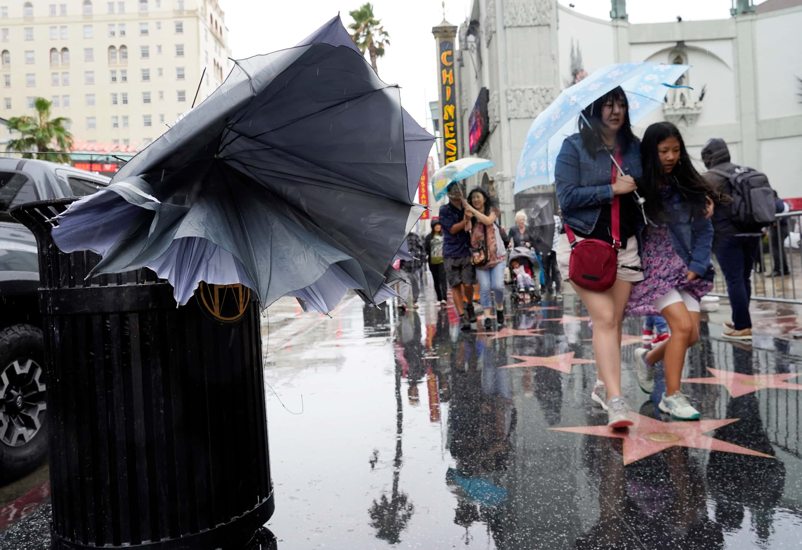 A broken umbrella protrudes from a trash barrel as pedestrians walk down Hollywood Boulevard...