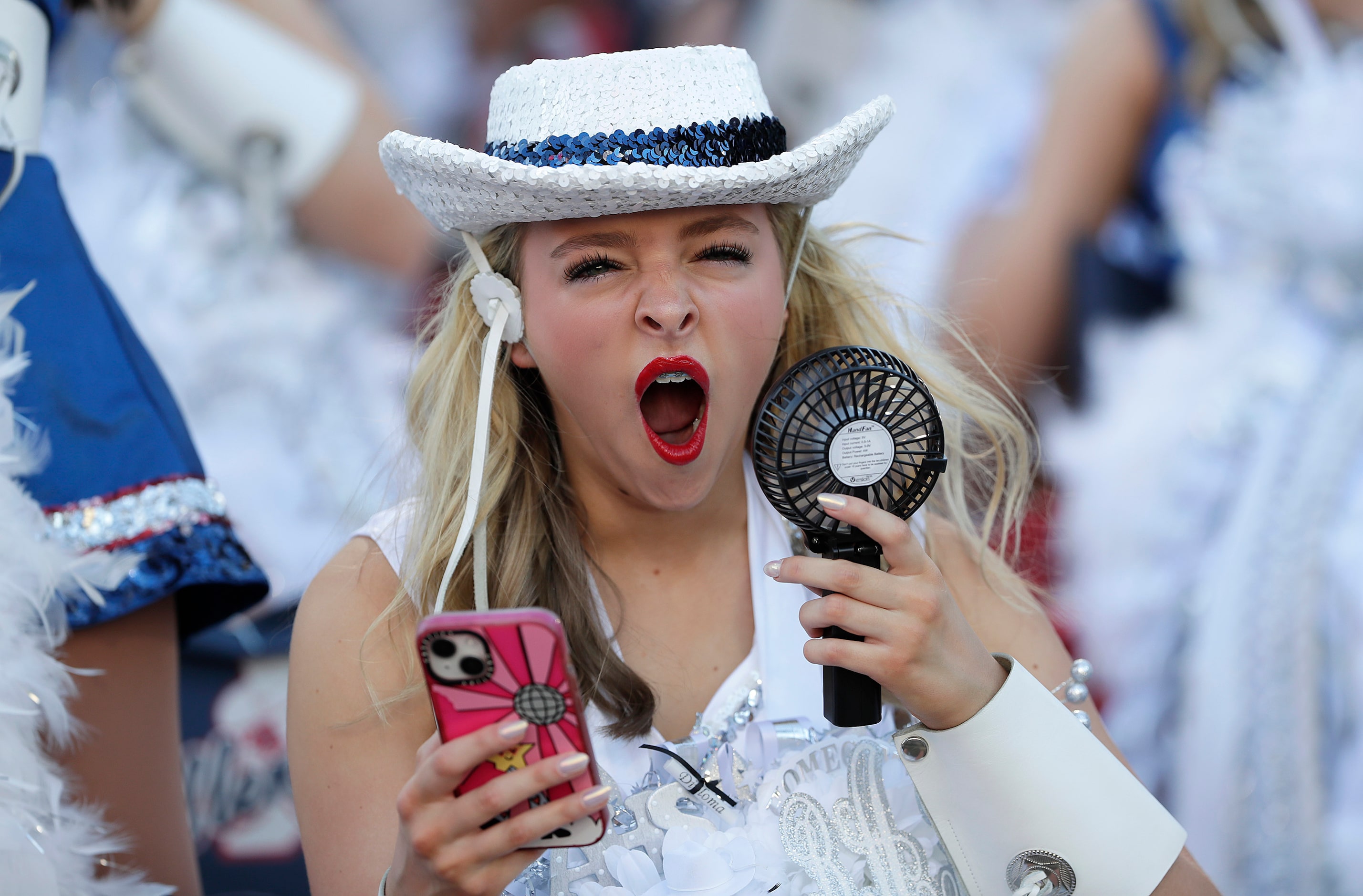 Brooklyn Ambrose, 17, with the Tallenettes drill team, yawn while using a portable fan...