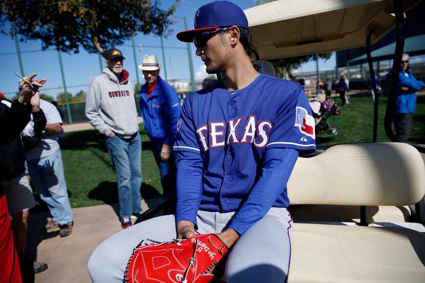 Texas Rangers pitcher Yu Darvish rides off on a golf cart after signing autographs following...
