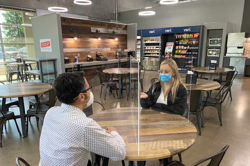 Employees in a break area at Vari headquarters in Coppell are separated by clear acrylic...