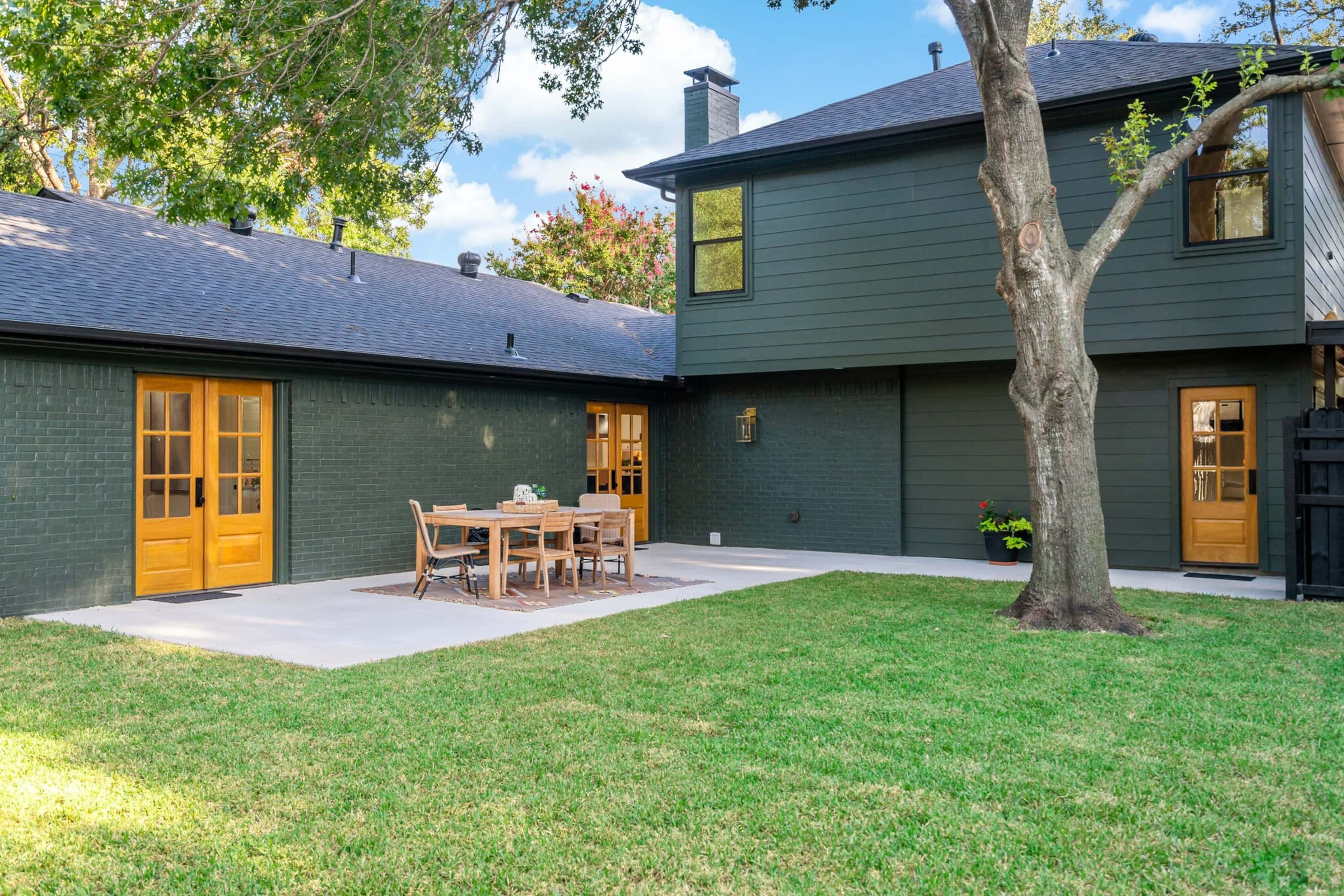 Backyard view of dark green house with large patio