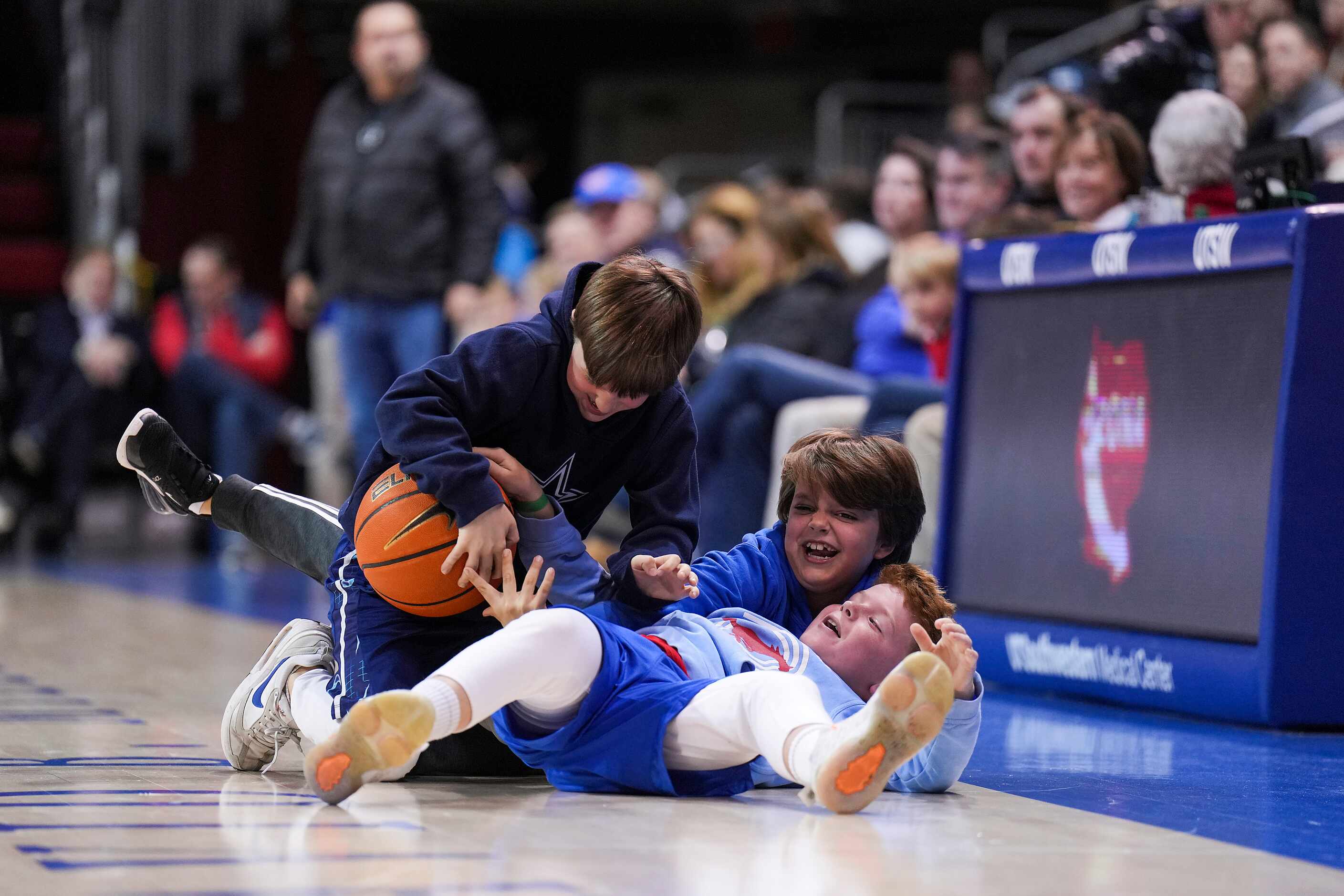 Young fans wrestle for a ball on the court during a timeout in an NCAA men’s basketball game...