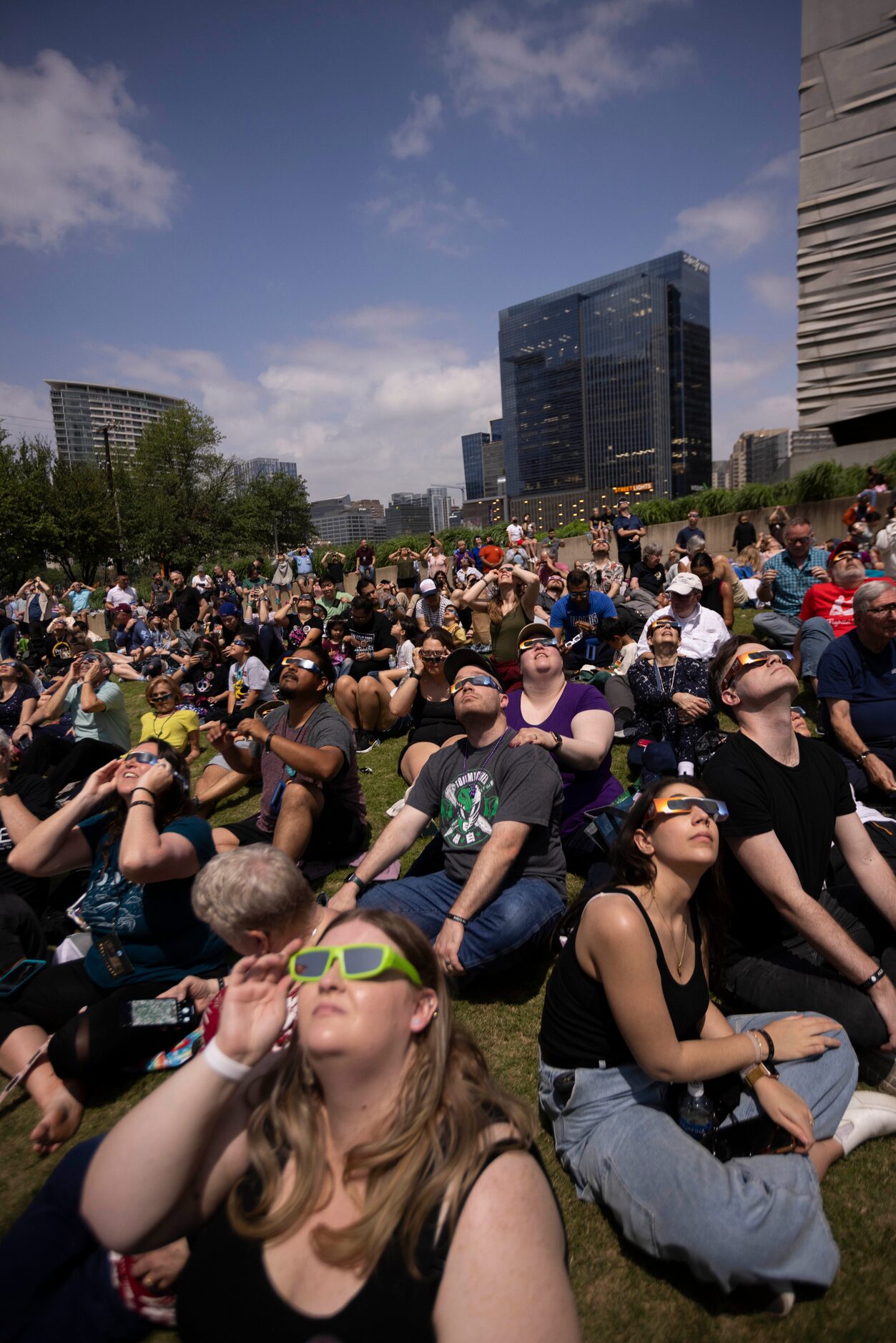 People watch the eclipse near totality as building lights turn on behind them during the...