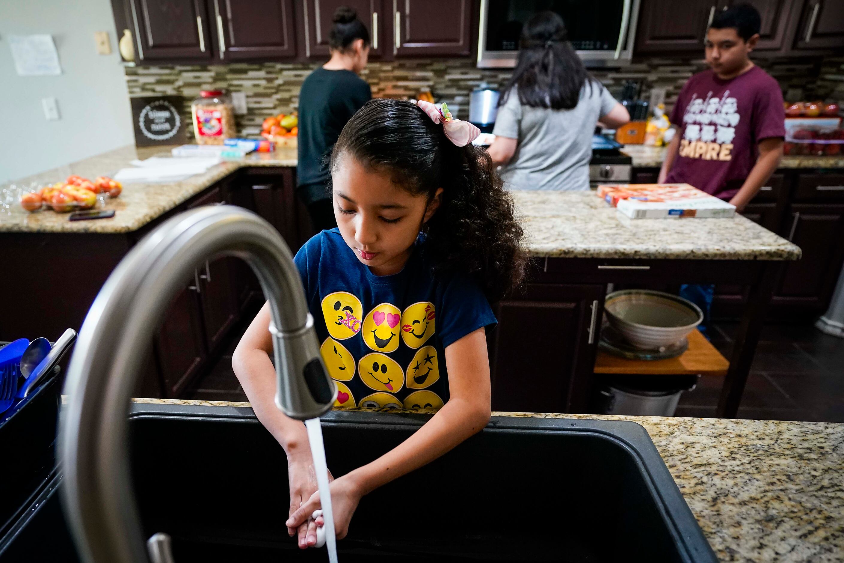 Selena Cabrera, 9, washes her hands as her mother Nancy Segovia-Cabrera (background center),...