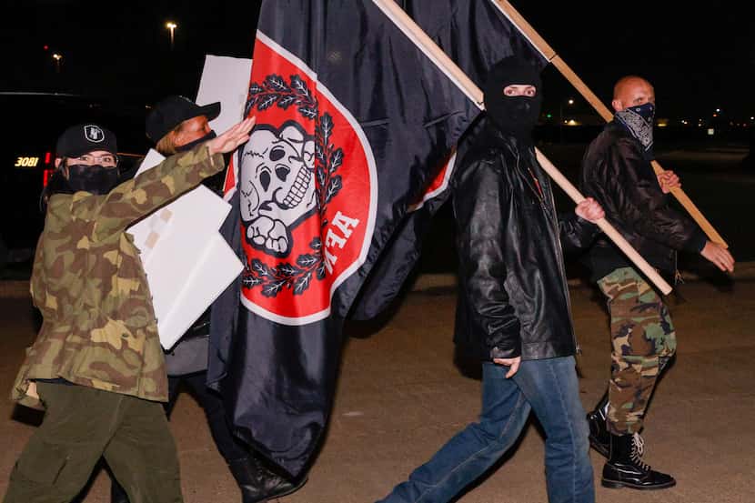 A member of the white nationalist Aryan Freedom Network (left) raises their arm in a Nazi...