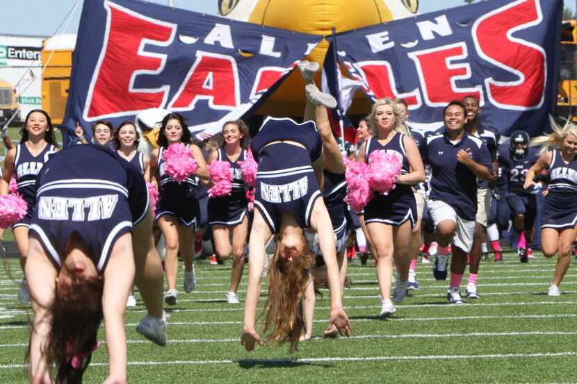 Allen Eagles cheerleaders lead their football team through the team inflatable and sign just...