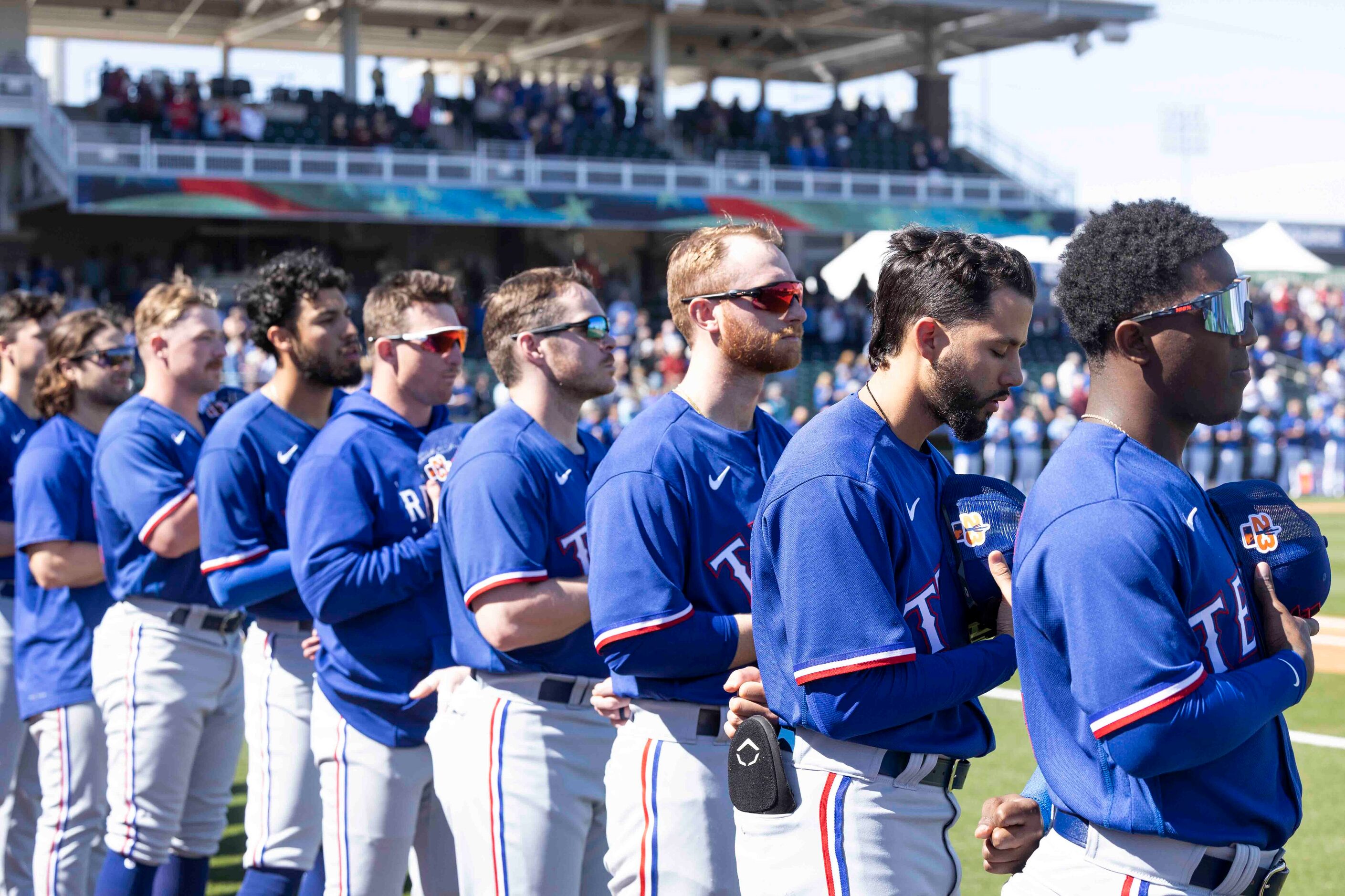 Texas Rangers players stand during the National Anthem at a spring training game against the...