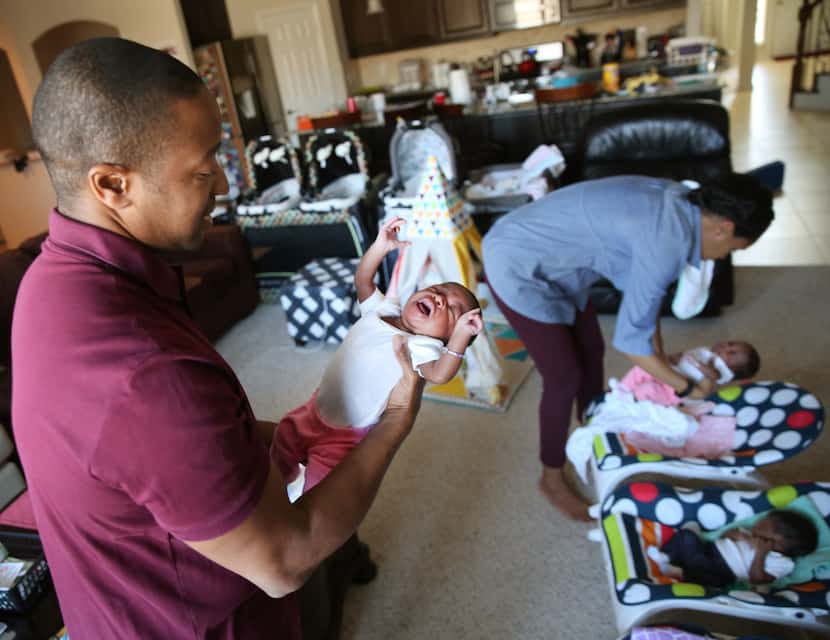 Gregory Hill holds one of his newborn triplets, Lena, while wife Kisha tends to Gemma and...