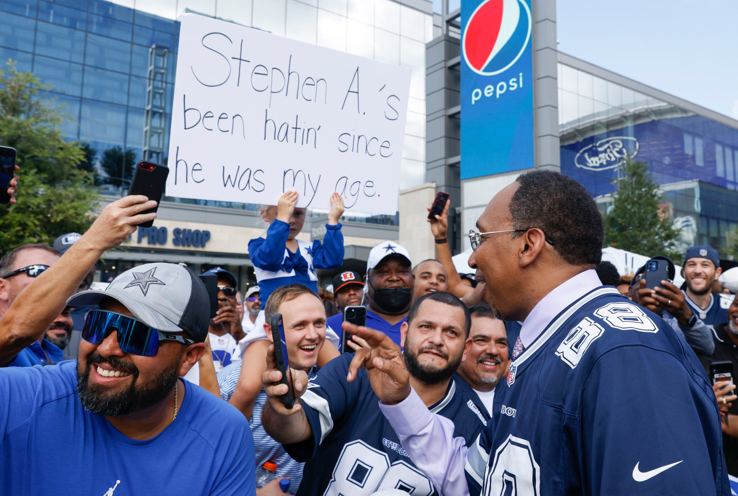 Host Stephen A. Smith also known as a "Cowboys Hater,” right, laughs as he passes by a sign...