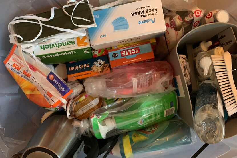 A box of supplies for Cooper's furnished apartment includes face masks, cleaning supplies,...