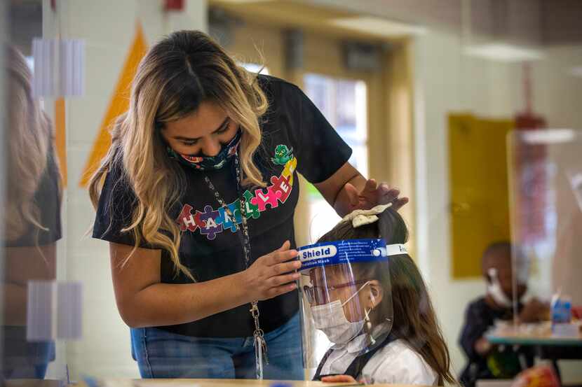 Pre-K 4 student Karen Martinez-Calderon (left) fastens a face shield onto Anastacia Valdez...