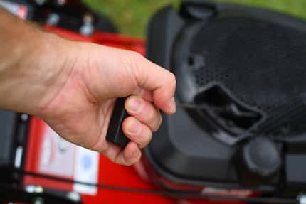 Man pulling a rip cord on a red lawn mower