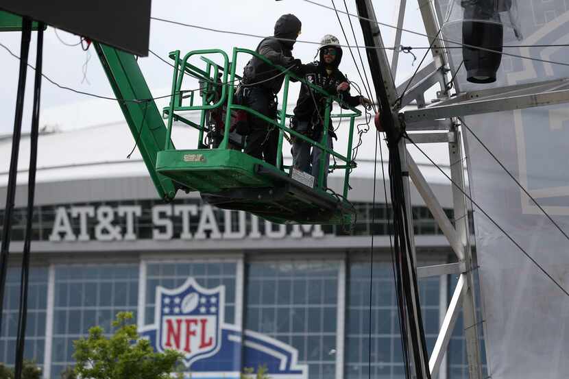 Workers secure a large video board above a walkway in preparation for the NFL Draft...
