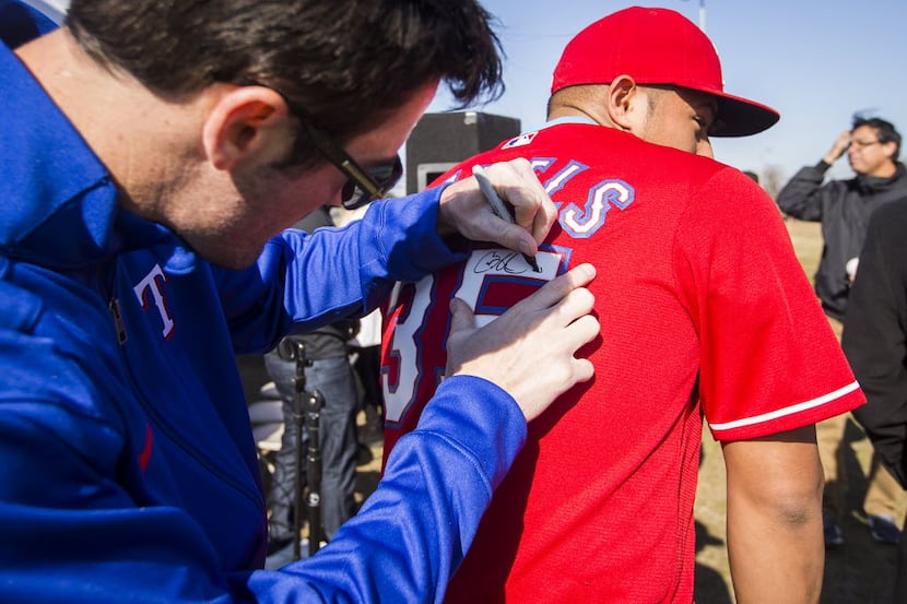 Texas Rangers pitcher Cole Hamels autographs a jersey bearing his name and number during a...