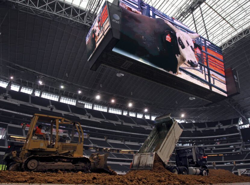 Some of 500 dump trucks filled with dirt transport their loads to the floor of AT&T Stadium...