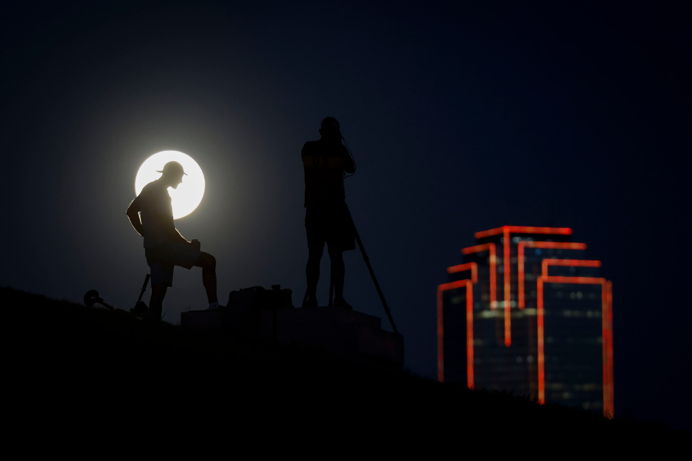 People gather as they watch and photograph the rise super harvest moon along the Dallas...