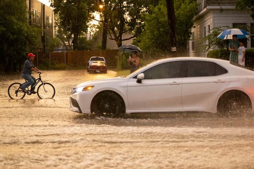 A man on a bike and drivers pass through a flooded section of the street at N Fitzhugh...