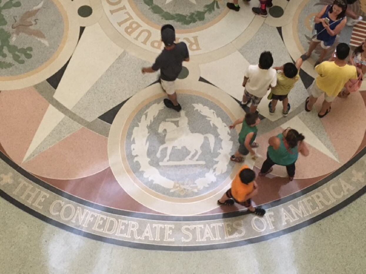 Tourists stride across the floor of the Capitol rotunda in Austin. The floor depicts seals...