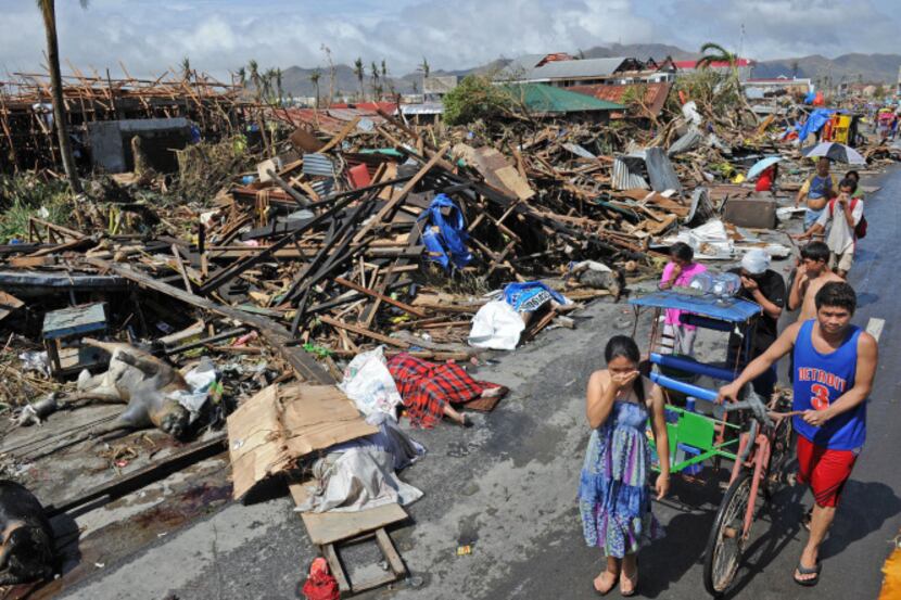 Survivors of Typhoon Haiyan walked past destroyed houses and dead bodies Sunday along a road...