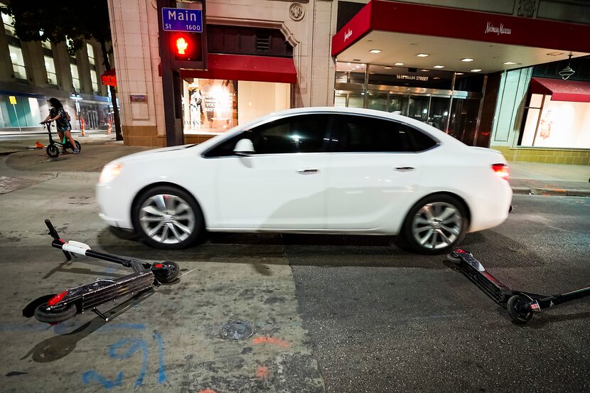 A car dodges rental scooters strewn across Main Street at Ervay in front of the Neiman...