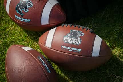 Logo footballs rest on the field during the first day of football practice for Frisco...