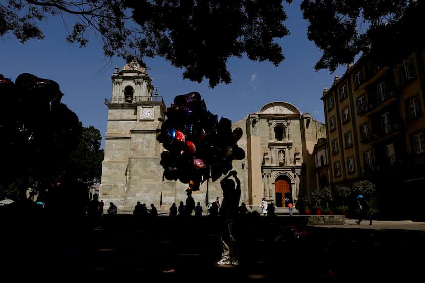 A balloon vendor is silhouetted against the Cathedral of Our Lady of the Assumption in Oaxaca.