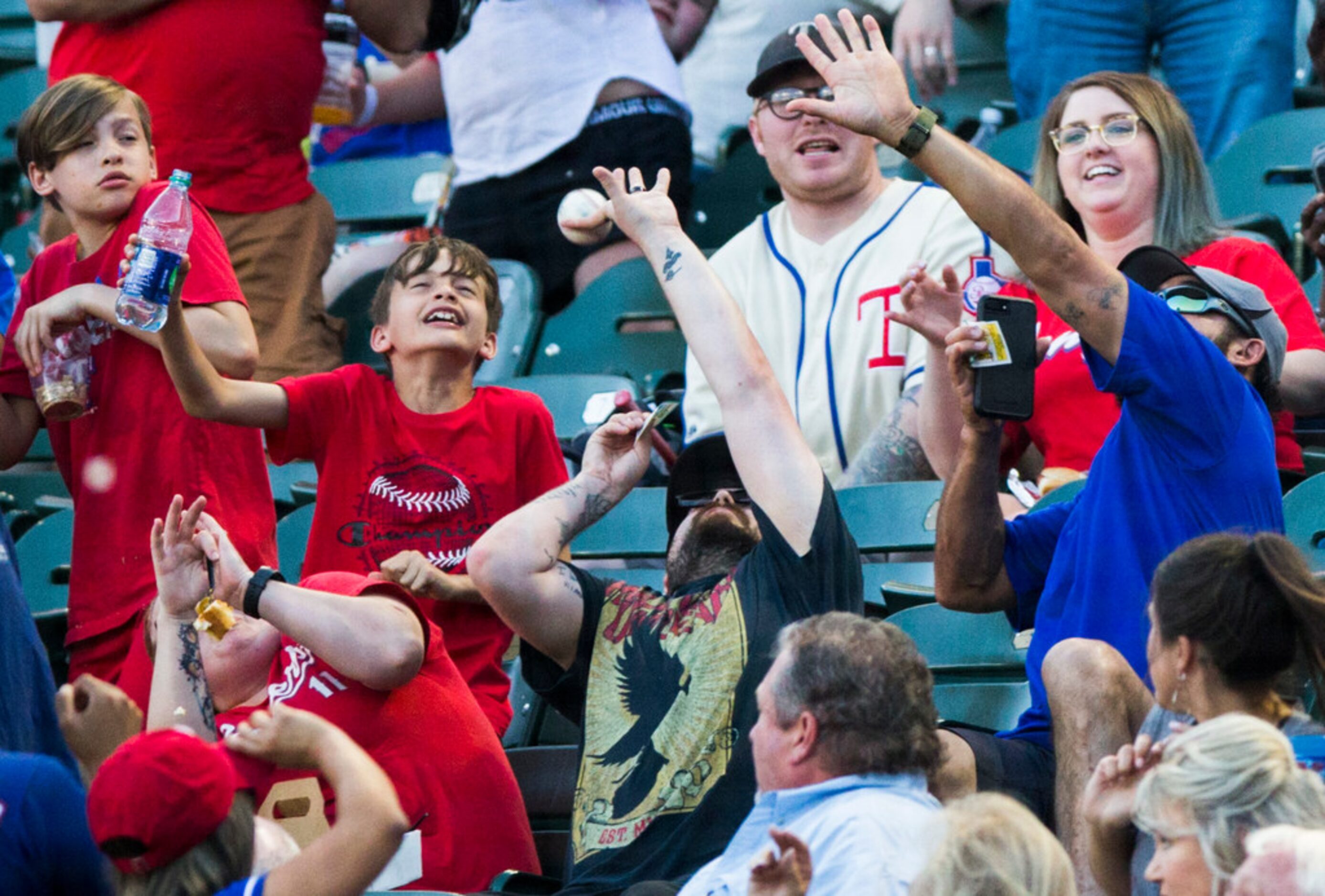 fans reach to catch a foul ball during the second inning of an MLB game between the Texas...