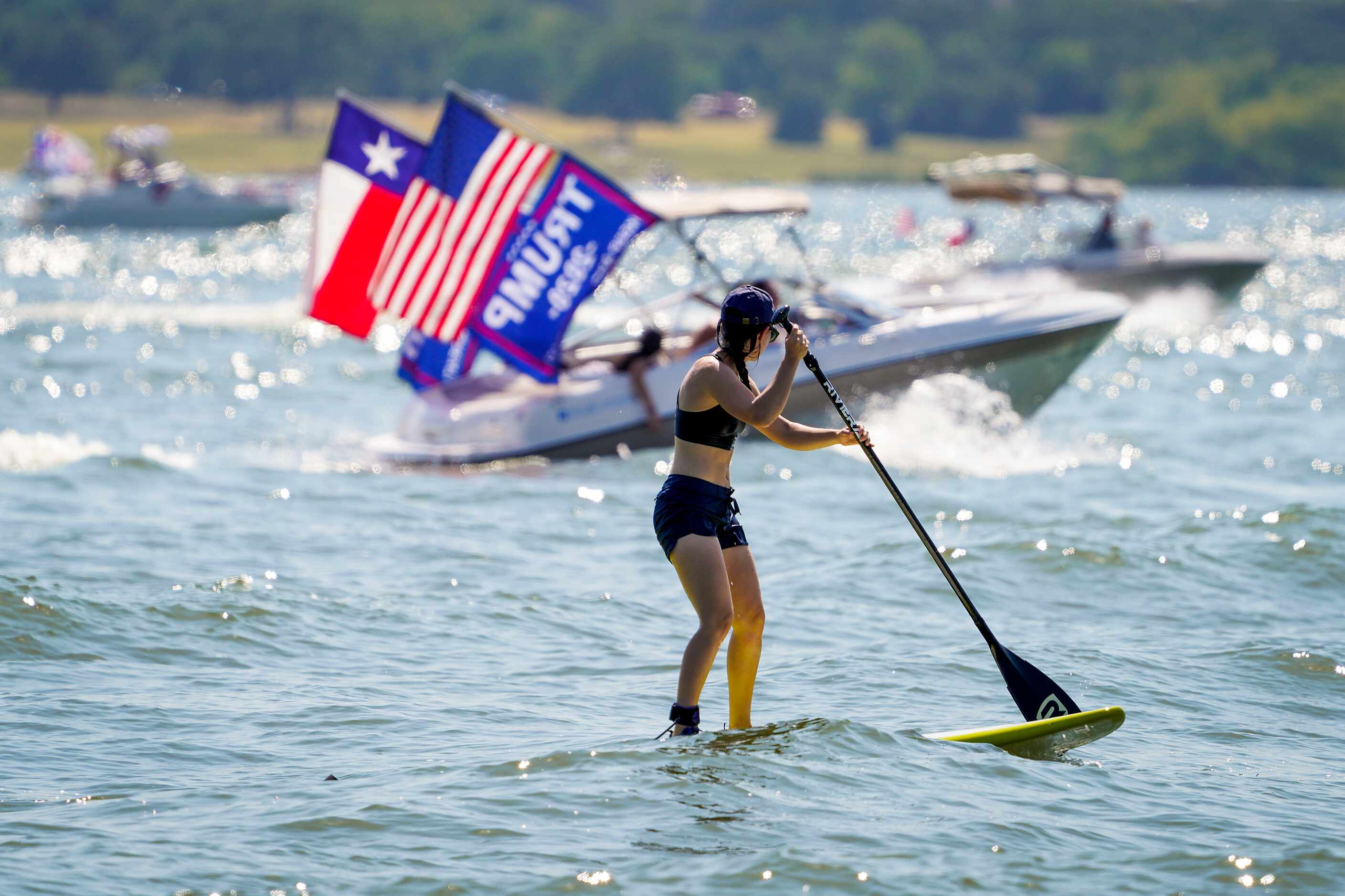 Boaters in support of President Donald Trump pass a woman on a paddle board as they parade...