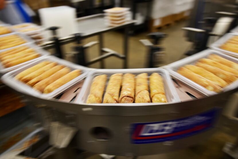 Egg rolls move on conveyor belts for packaging.
