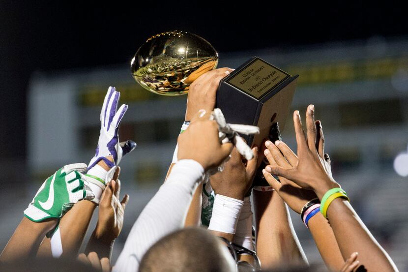 DeSoto players reach to touch the 6A Division 2 bi-district championship trophy after...