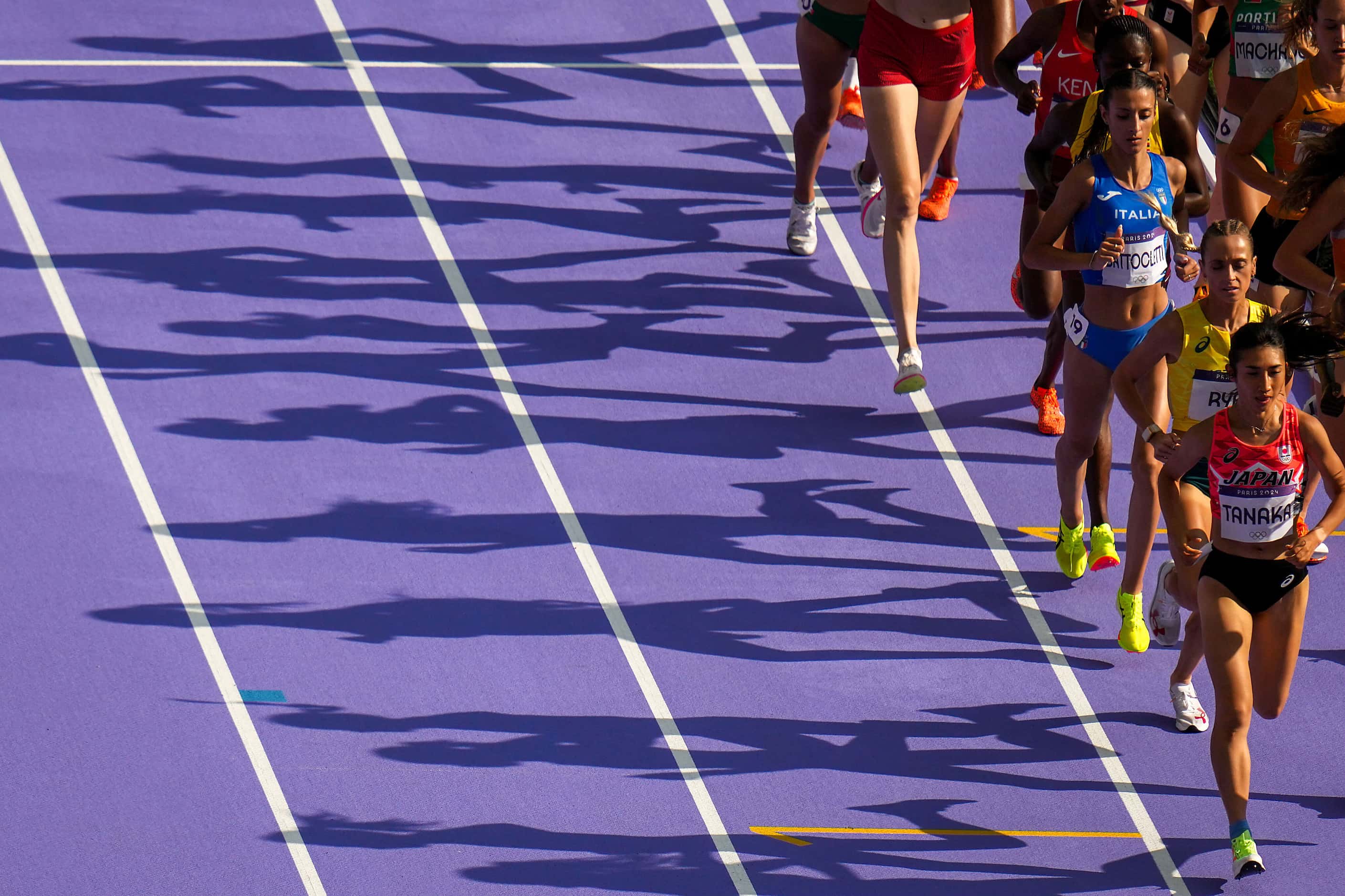 Runners cast shadows on the track during a heat of the women’s 5000-meters at the 2024...