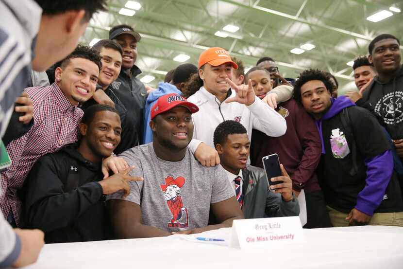 Allen football player Greg Little (center, in gray) is surrounded by teammates after signing...