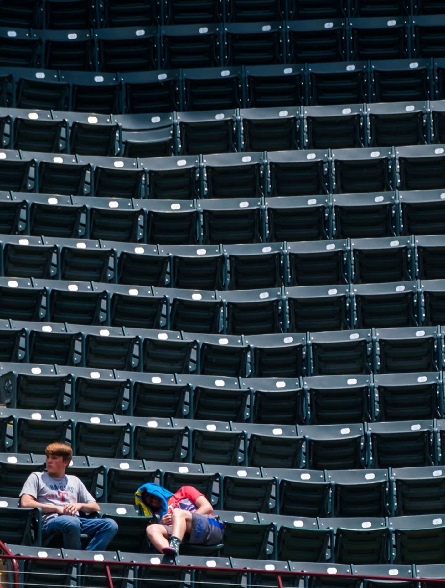 Fans sit in the sun amid empty seats as the Texas Rangers face the Seattle Mariners at Globe...