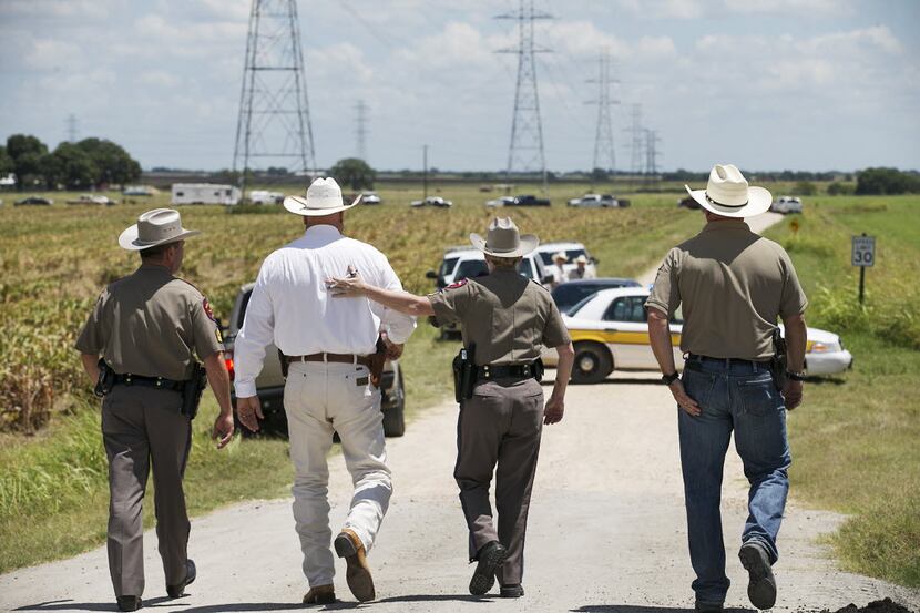 Texas DPS Trooper Robbie Barrera, center right, puts her arm around Caldwell County Sheriff...